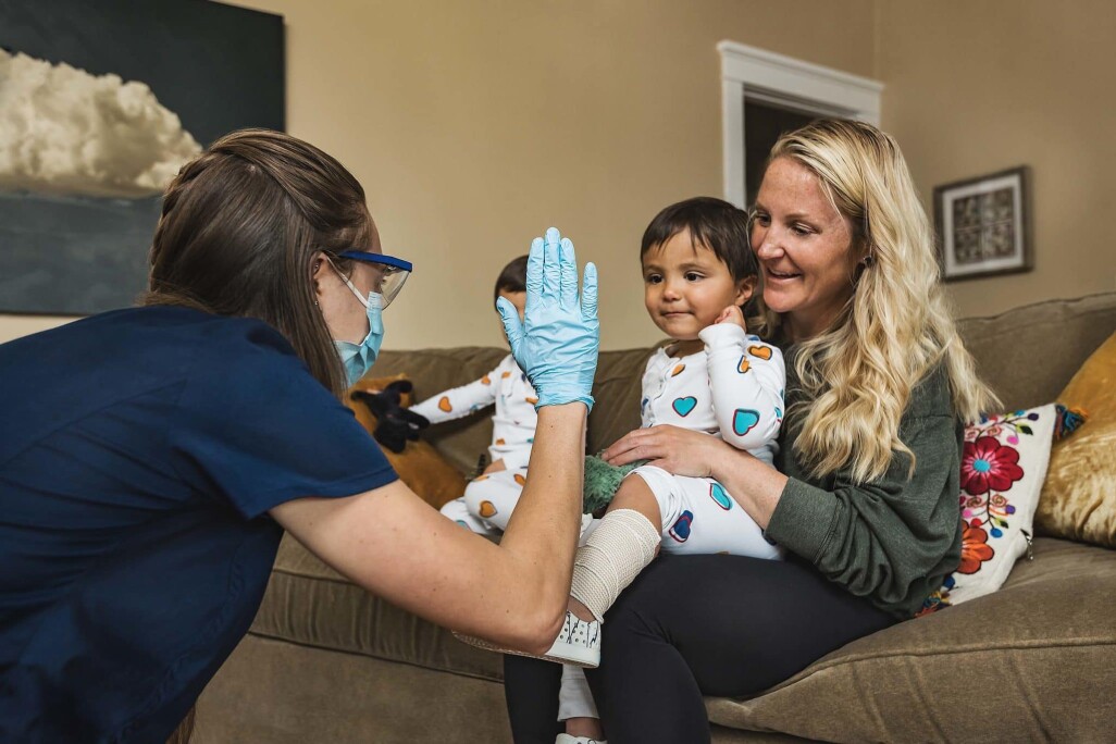 DispatchHealth provider high-fiving a young child sitting in their mother's lap