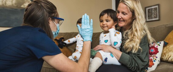 DispatchHealth provider high-fiving a young child sitting in their mother's lap