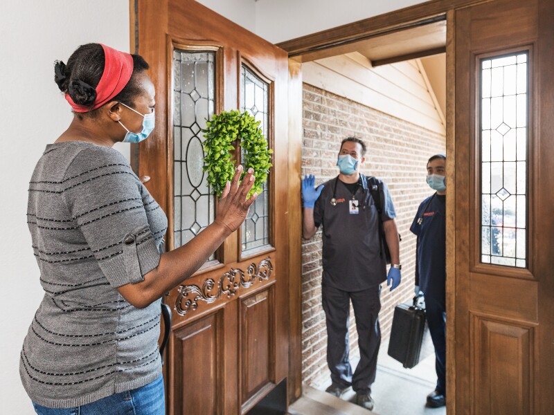 Woman in a mask welcoming masked DispatchHealth providers at her front door