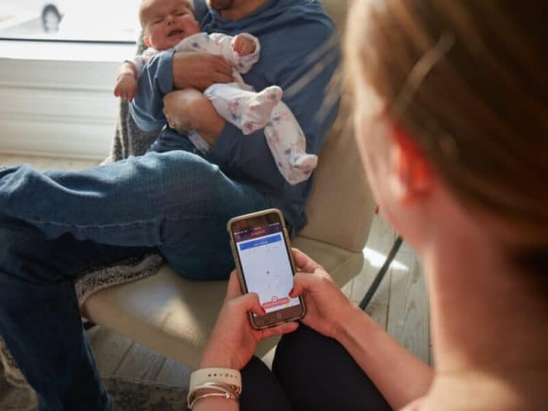 Man holding baby while woman uses DispatchHealth mobile app